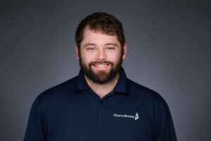 A man with a beard and blue eyes smiling at the camera, wearing a navy blue polo shirt with CleaverBrooks logo, set against a gray background.