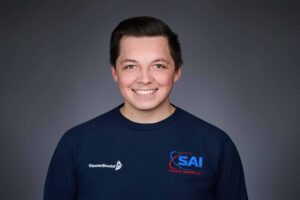 A young man with short dark hair is smiling at the camera. He is wearing a navy blue sweatshirt with the CleaverBrooks logo on one side and the SAI Stoermer-Anderson, Inc. logo on the other. The background is a soft gradient of dark gray tones.